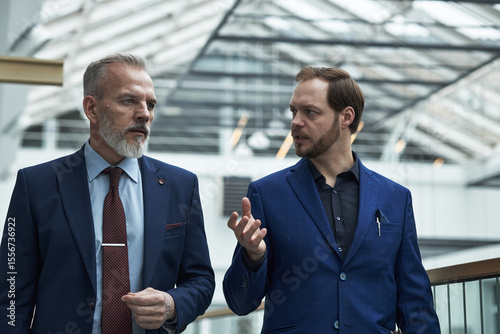 Obraz na płótnie Two Caucasian men in formal suits engaging in discussion while standing in a mod