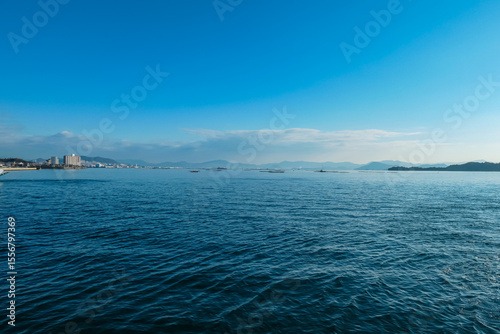 Calm blue sea stretches towards distant coastline and mountains near Miyajima, Japan. Serene seascape features traditional oyster farms, capturing tranquil beauty of the Seto Inland Sea on a clear day