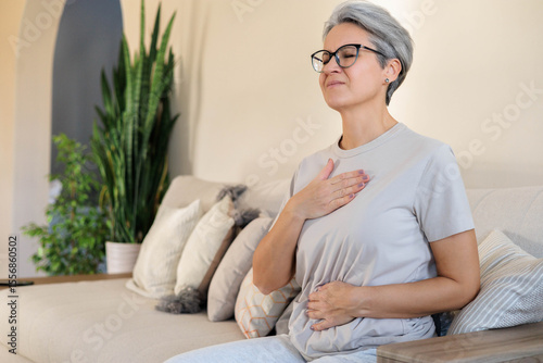Foto Senior woman feeling chest discomfort while sitting on sofa in cozy home environ
