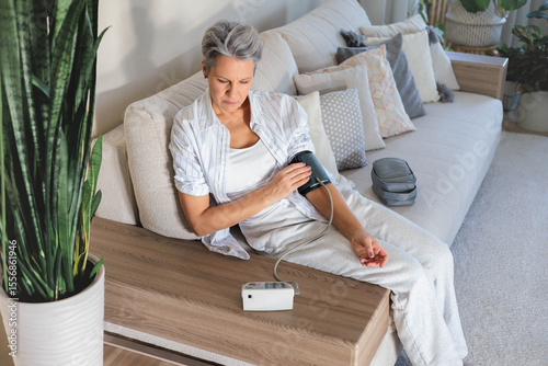 Senior woman checks blood pressure at home with digital monitor, daily health care routine photo