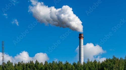 White industrial chimney emitting white smoke against a vibrant blue sky with fluffy clouds and green vegetation at the bottom. 