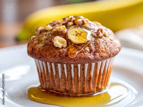 A single banana nut muffin on a white plate, drizzled with honey