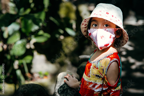 Little girl wearing hat, face mask and fancy dress in outdoor. R