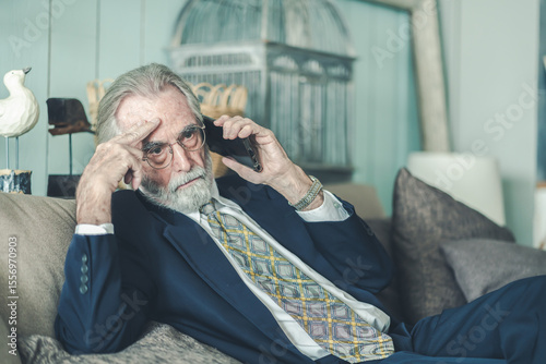 Senior businessman in formal shirt holding smartphone, appearing stressed during phone call lay off at old age, reflecting business crisis, financial worry or work-related anxiety, elderly healthcare