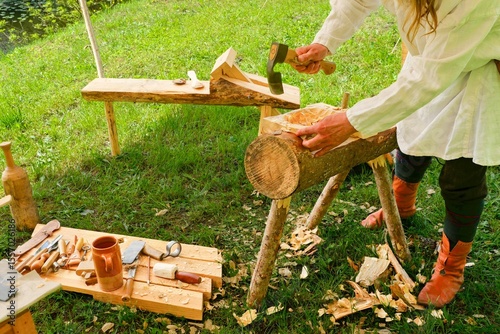Traditional Woodworking Craftsman Using Axe and Adze. Man in Historical Costume Carving Wooden Log.