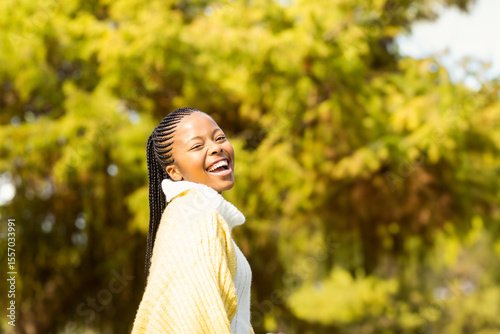 African American woman laughing while looking over shoulder in sunny park wearing sweater and shawl