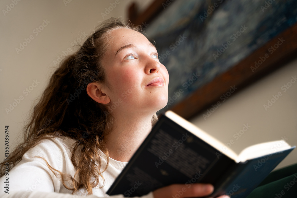 Pensive young woman with book looking at window with thoughtful expression in living room at home in daylight, resting relaxing and spend free time indoors, weekend leisure alone, low-angle portrait Pensive young woman with book looking at window with thoughtful expression in living room at home in daylight, resting relaxing and spend free time indoors, weekend leisure alone, low-angle portrait