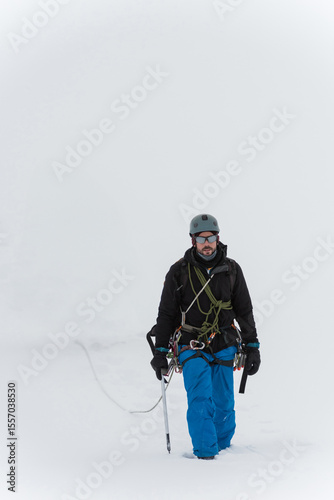 Mid adult man traversing snowy glacier wearing climbing gear and carrying rope and backpack