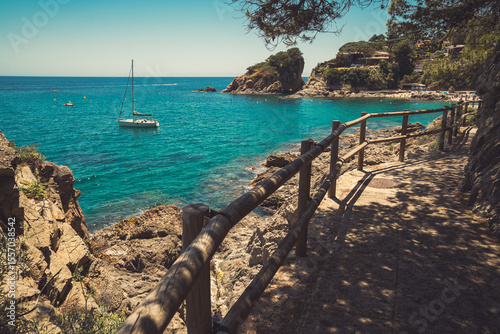Cuadro en lienzo Seascape in Blanes, Spain with a sailboat in the background and a promenade on a cliff called Cami de Ronda in the foreground