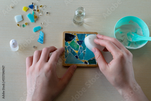 Final adjustments to handmade mosaic plaster coaster in silicone mold with faux glass fragments and white gypsum compound before it hardens, step 4