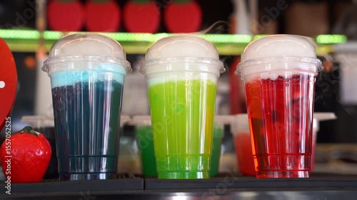 trio of colorful carbonated drinks in plastic cups with dome lids blue green red fizzy beverages on bar counter at outdoor food market summer street festival soda refreshment variety vibrant display