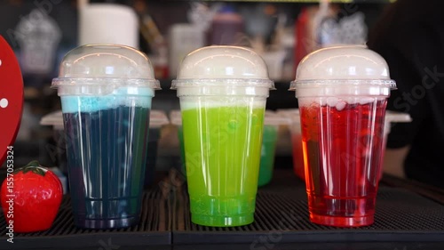 trio of colorful carbonated drinks in plastic cups with dome lids blue green red fizzy beverages on bar counter at outdoor food market summer street festival soda refreshment variety vibrant display