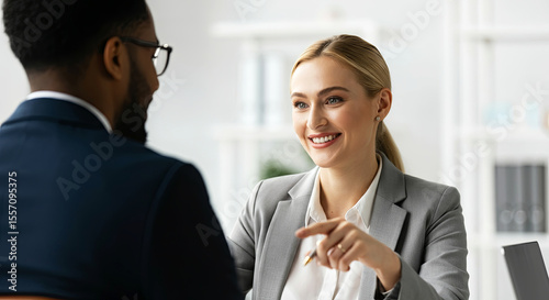 Businesswoman in gray suit engaging in conversation with male colleague in office setting, showcasing professional interaction and collaboration in a modern workspace