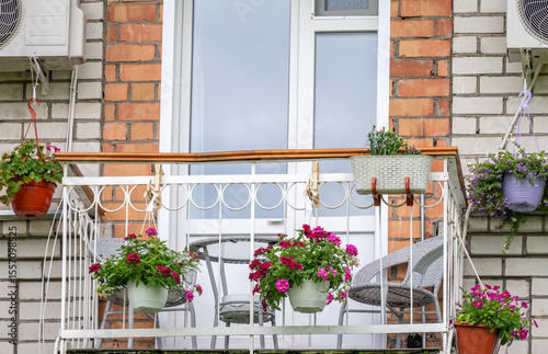 Balcony of an apartment building with a table and chairs decorated with flowers in pots and boxes.