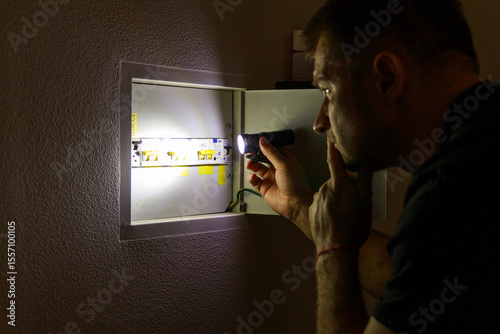 Power outage. A man holds an LED lamp in front of an electrical panel.