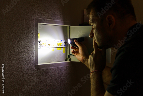 Power outage. A man holds an LED lamp in front of an electrical panel.