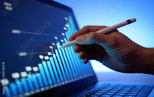 Hand using stylus to analyze rising bar graph on laptop screen