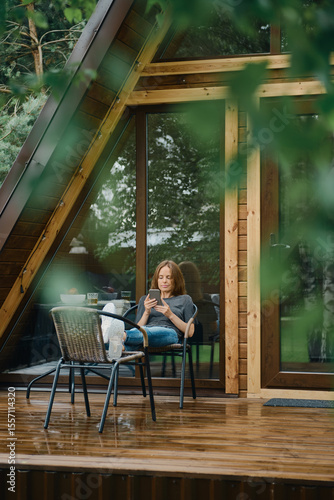 Pretty woman reading in smartphone outside a modern wooden cabin