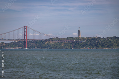 View of the 25 de Abril Bridge and the Cristo Rei monument across the Tagus River, photographed from Lisbon, Portugal, on June 13, 2025, on a clear day with calm water.
