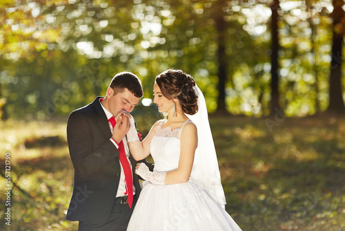 A bride and groom are standing in a field, with the bride wearing a white dress