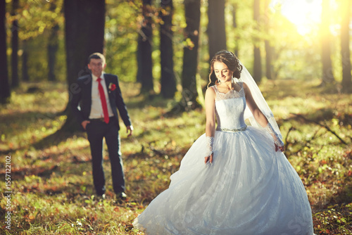 A bride and groom are walking through a forest