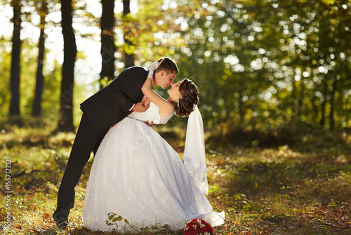 A bride and groom are kissing in the woods
