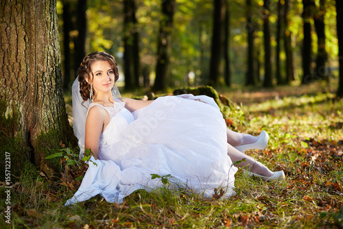A woman in a white dress is sitting on the ground in a forest