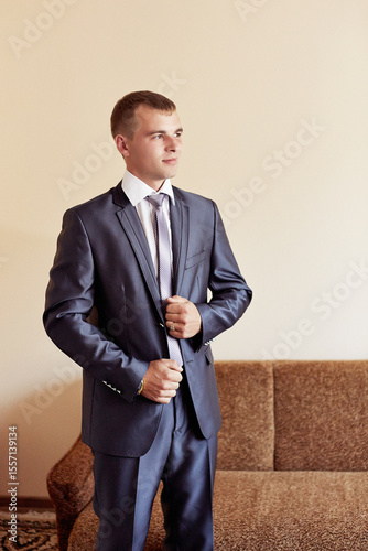 A man in a suit and tie is standing in front of a couch