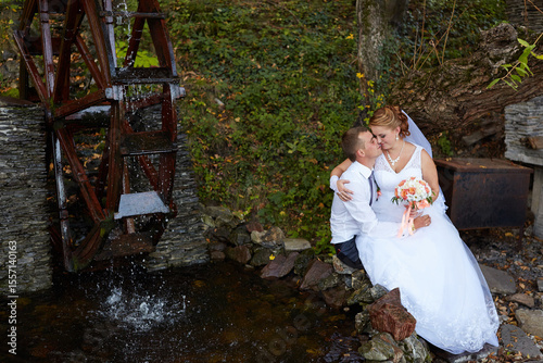 A bride and groom are sitting on a rock near a water fountain
