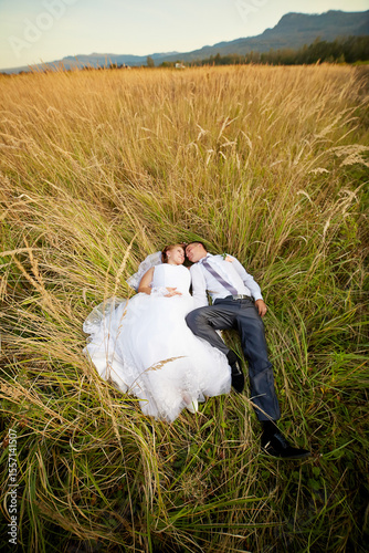 A bride and groom are lying in a field of tall grass