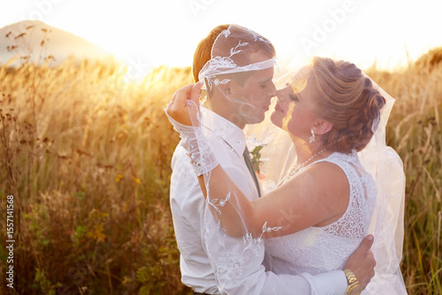 A bride and groom are embracing in a field of tall grass