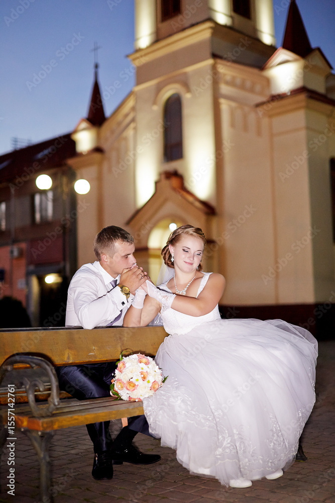 Fototapeta premium A bride and groom are sitting on a bench outside a church