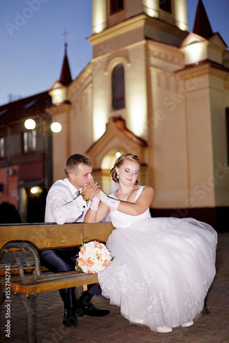 A bride and groom are sitting on a bench outside a church