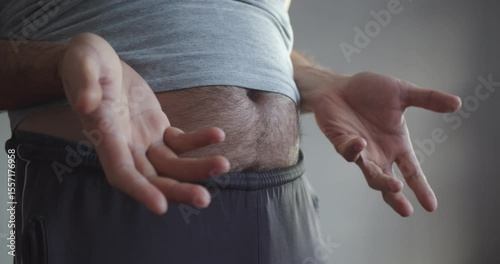 Modern Adult man in sweatpants and a T-shirt with a bare hairy beer belly actively gesticulates. Close-up on the stomach and arms