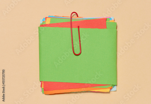 Stack of multi-colored sticky notes secured with a red paper clip, placed on a beige background.
