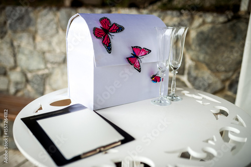 Butterfly wedding card box. A stylish wedding card box adorned with butterflies sits on a table beside champagne glasses and a guest book.