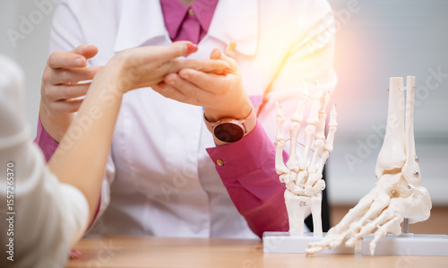Female doctor examines patient's hand with bone models in medical rheumatology office