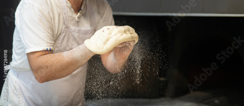 Male hands shaping famous flat bread pide dough splashing flour particles in front of a wood burning fire in a traditional bakery in Turkey