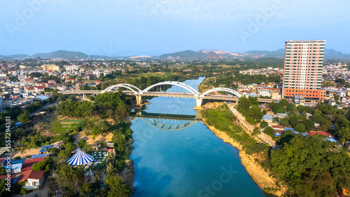 Aerial view of the Ben Tuong Bridge, an arch bridge spanning the Cau River in Thai Nguyen city, with its reflection in the water.
