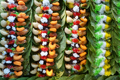 Close-up of colorful paan preparations on betel leaves, arranged in rows, showcasing various sweet treats and spices.