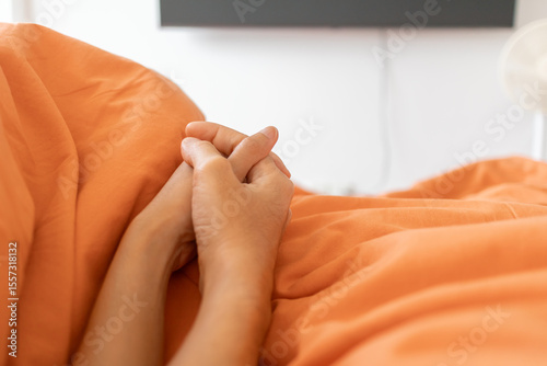 Asian couple holding hands under orange blanket in bed
