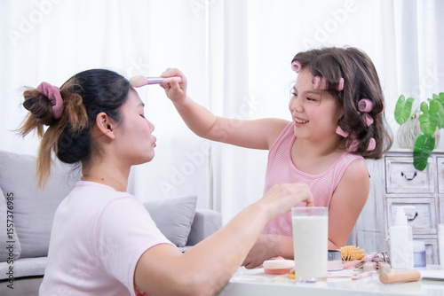 Kids, cosmetic, child, beauty, makeup, A young girl with curlers happily applies blush on her mother’s face during a fun moment, highlighting creativity, bonding, and expression in home life.