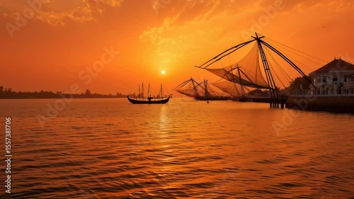 Traditional Chinese fishing nets line the shore at sunset in Kochi, Kerala, casting silhouettes over the glowing orange water.