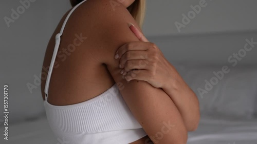 Young woman pinches soft fat area on her upper arm, showing concern about flabby skin, weak triceps and excess weight. Body insecurities, real beauty, vulnerability, imperfections, problem zones