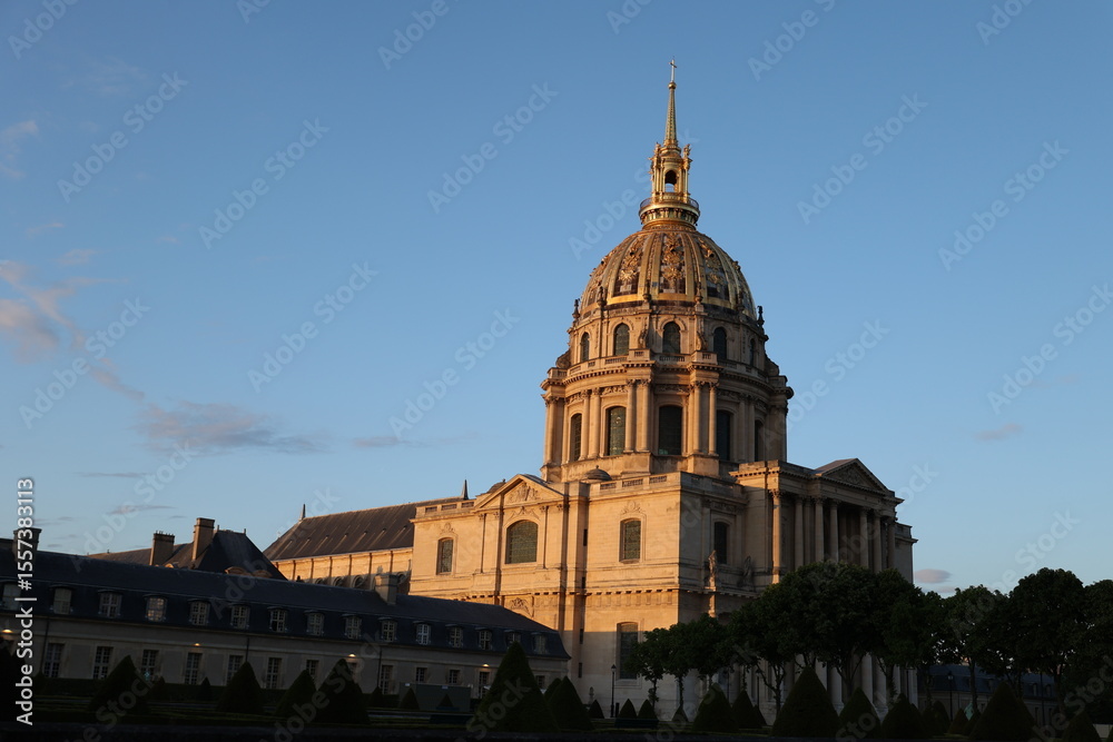 Obraz premium The grand golden dome of Les Invalides in Paris gleams under the warm light of golden hour. This iconic French landmark showcases magnificent classical architecture against a clear blue sky.
