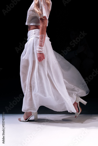 Cropped female figure dressed in a chic fancy blouse and long white skirt walking on black background. 