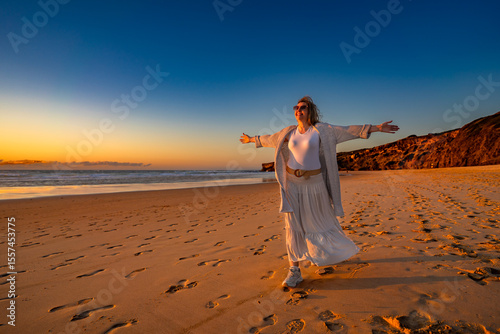 Beautiful mid adult woman enjoying walk on sandy beach on sunset on windy spring day. Front view. Monte Clerigo beach on Algarve coast in Portugal	