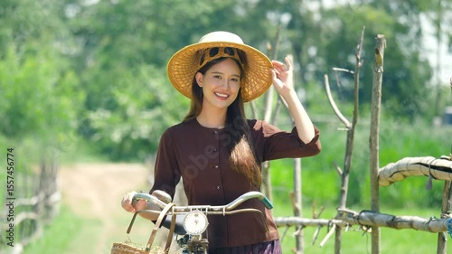 Footage 4 k resolution. Portrait of young woman wearing a traditional hat in a rice field. Beautiful Asian woman with old bicycle walking in field, outdoors
