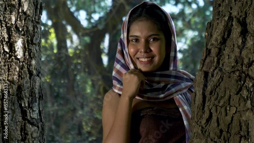 Portrait Asian woman smiling with Thai loincloth covers head standing near a big tree in the forest