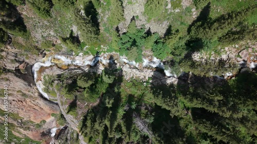 Crystal clear water cascading through rocky gorge, winding between lush green vegetation and revealing pristine wilderness landscape under bright sunlight